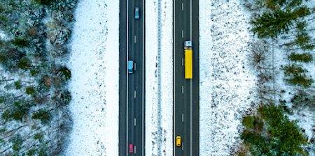 Vehicles traveling on a two-lane highway through a forest in winter.