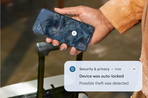 A smartphone displays a security notification that reads, 'Device was auto-locked. Possible theft was detected'. The phone is being held in a hand near the handle of a rolling suitcase.
