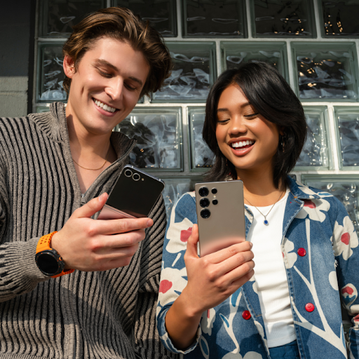 Two people standing together outside, both looking at their Android phones.