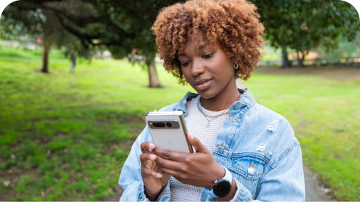 A woman in a park holding a smartphone.
