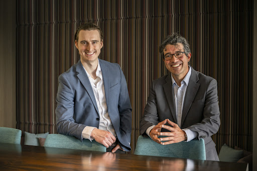 Two men stood behind the chairs and posing for picture.