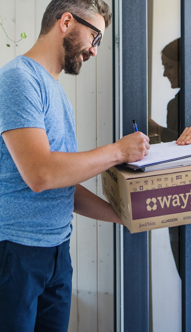 A woman delivering a Wayfair package to a man signing for it