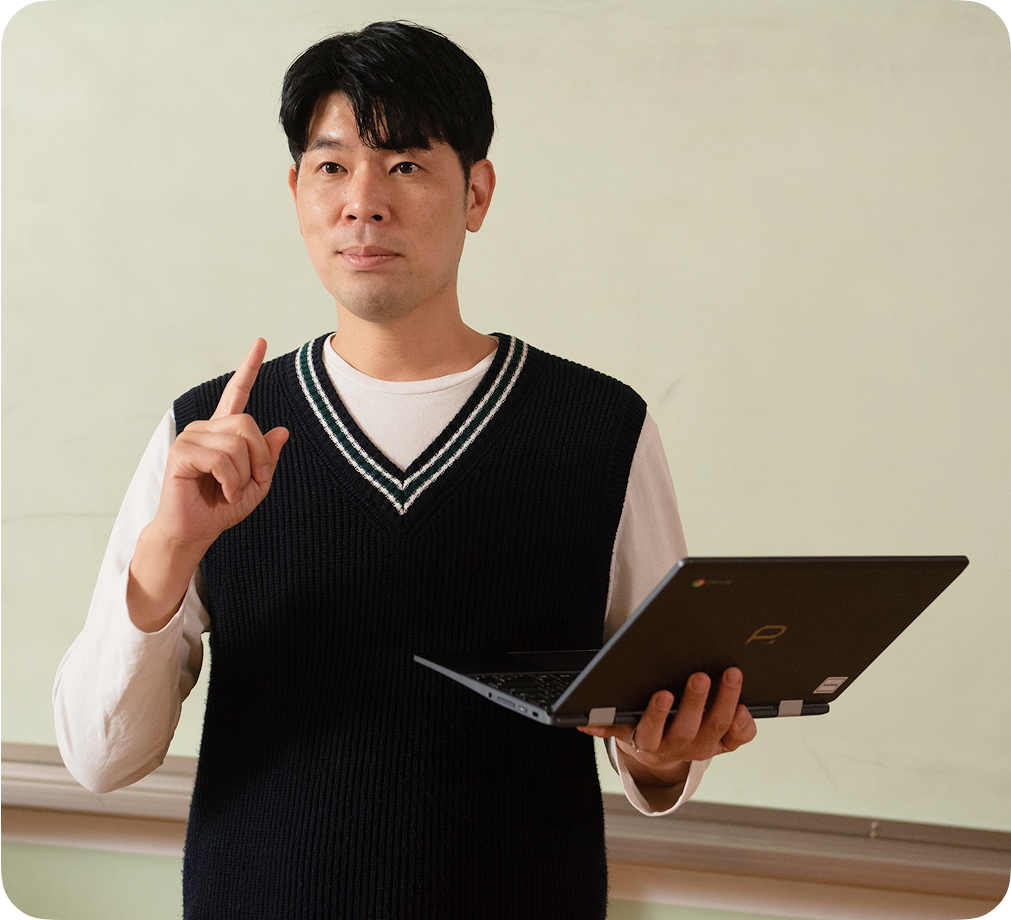 교실 앞에 서서 한 손으로 열려 있는 Chromebook 기기를 든 젊은 교사