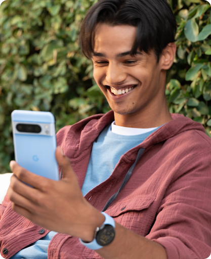 Man is sitting down in a chair and smiling while looking at his Pixel 9 phone.