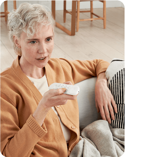 A woman using a Google TV remote and Google Assistant to dim the lights