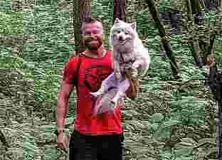 A photo of Rusty, who is a strong young man wearing a red t-shirt, holding his fluffy white dog in one arm.