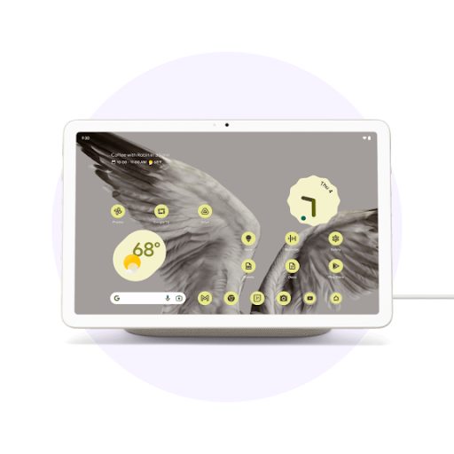 A white tablet on a charging dock with a cable. Its screen shows an abstract bird image and multiple interface icons.